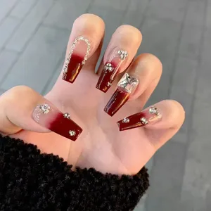 Uñas postizas largas degradadas rojas con diamantes de imitación y detalles de lujo.