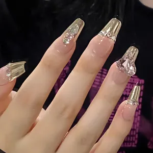 Primer plano detalle de uñas postizas largas de lujo con puntas doradas y pedrería de cristal.
