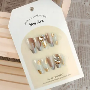 Detalle en primer plano de uñas postizas de lujo con degradado marrón, pan de oro y pedrería.