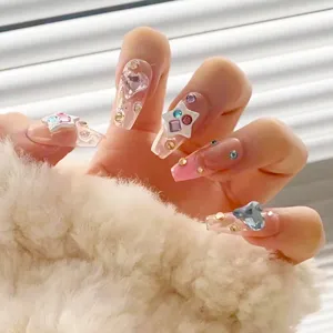 Vista detallada de uñas postizas transparentes con estrellas 3D y brillantes pedrerías de colores.