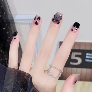 Primer plano detallado de uñas postizas hechas a mano con lazos negros y anillo.