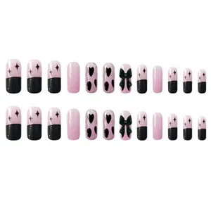 Vista detallada de uñas postizas lindas con un lazo negro y bonitos diseños de corazones.