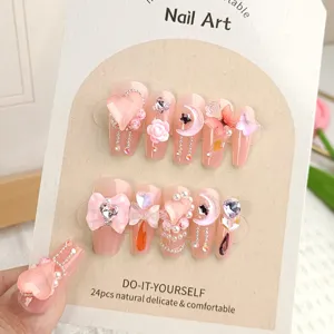 Gros plan d'ongles press-on roses 3D avec joli nœud papillon et pendentif cœur en cristal.