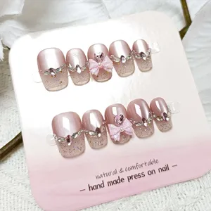 Uñas postizas hechas a mano con purpurina cat-eye larga, pedrería brillante y bonitos lazos rosados.