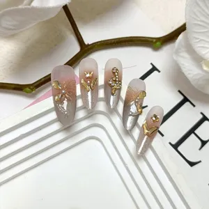 Detalle de uñas postizas hechas a mano, gel cat-eye con dijes dorados de mariposa y serpiente.