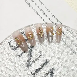 Detalle de uñas postizas hechas a mano con efecto ojo de gato, dijes de serpiente y estrás.