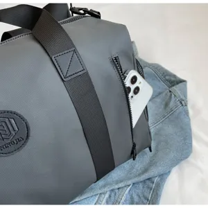 Close-up of grey travel duffel bag with side zipper pocket holding smartphone and black straps.