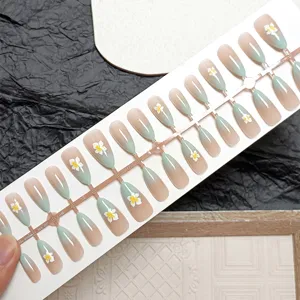 Close-up detail view of almond press-on nails with green gradient and 3D white floral design.