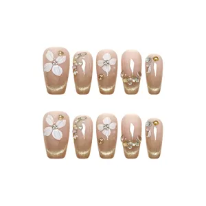 Uñas postizas hechas a mano con flores blancas, degradado con purpurina y pedrería brillante.