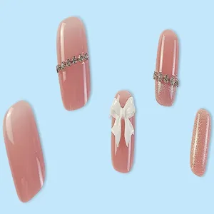 Primo piano dettagliato di unghie finte nude cat-eye con fiocco bianco 3D e catena di strass.