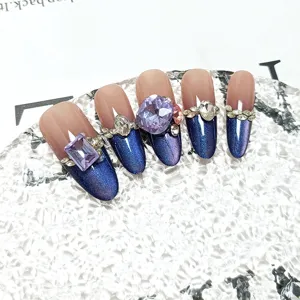 Handgemaakte lange neppe nagels met kattenoog gel en grote kristallen voor een mooie manicure.