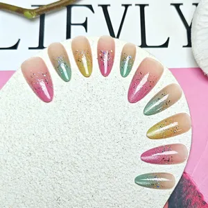 Primo piano di unghie finte a mandorla fatte a mano con sfumatura colorata e glitter effetto cat-eye.
