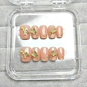 Primer plano detallado de uñas postizas con base degradada nude y dijes de mariposa dorados.