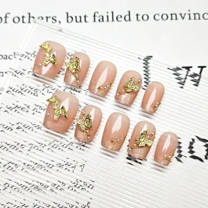 Uñas postizas nude decoradas con mariposas doradas, perlas y elegante diseño cat-eye.