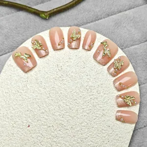 Detalle de uñas postizas hechas a mano estilo ojo de gato nude con mariposas doradas y perlas.