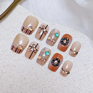 Detalle en primer plano de uñas postizas con diseño de cuadros, lazo y rosquilla.