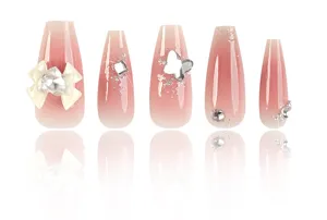Detailopname van lange neppe nagels met roze ombré, strik en glimmende strasssteentjes.