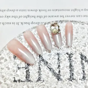 Uñas postizas largas ovaladas con degradado rosa nude efecto ojo de gato y pedrería fina.