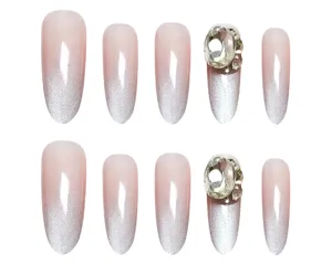 Detalle en primer plano de uñas postizas ovaladas largas con efecto ojo de gato rosa nude y pedrería.