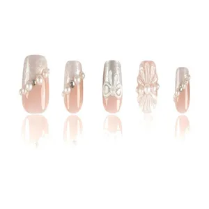 Detalle en primer plano de uñas postizas con lazo de perlas 3D y flores de cristal elegantes.