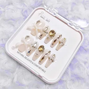 Detalle cercano de uñas postizas largas de lujo con lazos blancos y cristales brillantes.