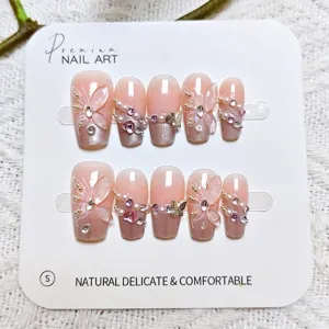 Primer plano detallado de uñas postizas rosas hechas a mano con mariposas y perlas.