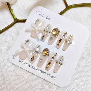 Exquisitas uñas postizas largas con pedrería brillante, perlas y lazo elegante para un estilo único.