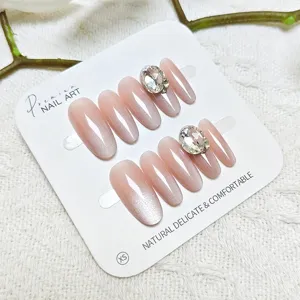Detalles de uñas postizas nude con degradado ojo de gato y brillantes pedrerías.
