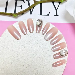 Vista detallada de uñas postizas degradadas en rosa nude con ojo de gato y cristales brillantes.