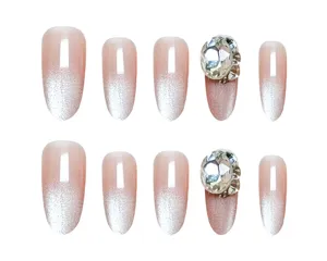 Vista detallada de uñas postizas con degradado rosa nude efecto ojo de gato y pedrería brillante.