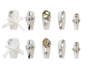 Detalle de uñas postizas largas con brillantes diamantes de imitación y delicados lazos blancos.