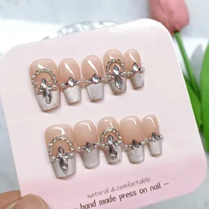 Detalle de uñas postizas hechas a mano con pedrería de lujo y puntas francesas brillantes.