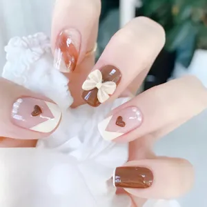 Detalles de uñas postizas hechas a mano, diseño marrón y blanco con elegante lazo y perlas.