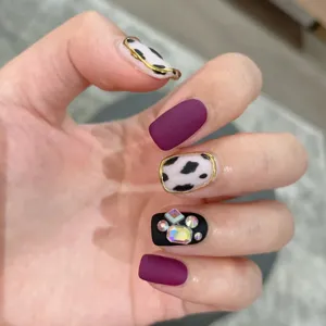 Uñas postizas hechas a mano con morado mate, diseño de vaca, líneas y estrás brillantes.