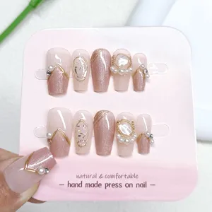 Detalle de uñas postizas hechas a mano efecto ojo de gato con perlas brillantes y hilos dorados.