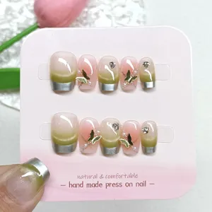 Primer plano de uñas postizas hechas a mano con degradado ojo de gato verde y mariposas doradas.