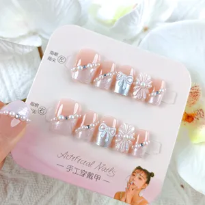 Detalle de uñas postizas hechas a mano con lazo de perlas y diseño de flores de cristal.