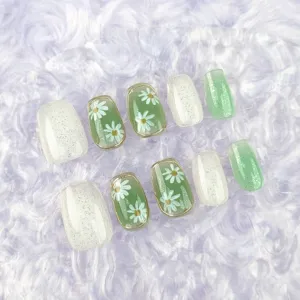 Primer plano de uñas postizas hechas a mano con diseño de margaritas y purpurina verde.