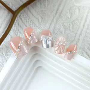 Detalles de uñas postizas hechas a mano con lazo 3D, perlas y relieve de flor de cristal en rosa nude.