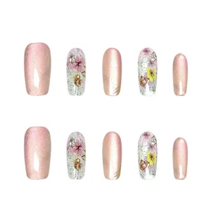 Vista detallada de uñas postizas de ojo de gato rosa con elegantes adornos florales y pedrería.