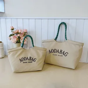 Detailopname van een beige canvas shopper met groen touw handvat en handgemaakte print.