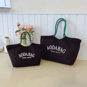 Zwarte canvas tote bag set met groene touw handvatten en een witteletter opdruk.
