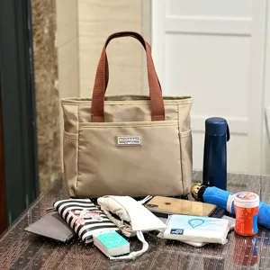 Detailed view of casual beige commuter tote bag with brown handles and multi-pocket design.