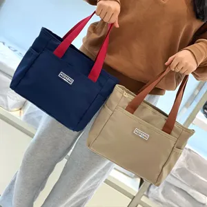 Detail view of the contrast color canvas tote bag, featuring dual top handles and front pocket storage.