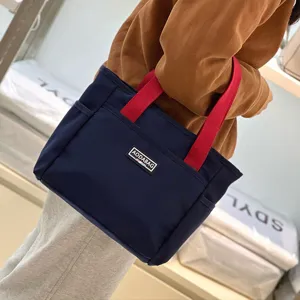 Detailed view of the stylish dark blue tote bag with red handles and a front storage pocket.