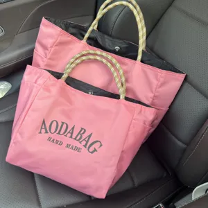 Detail shot of the pink canvas tote bag showing textured rope handles and black logo print.