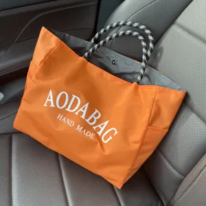 Orange nylon tote bag detail showing black white pattern handles and large capacity compartment.