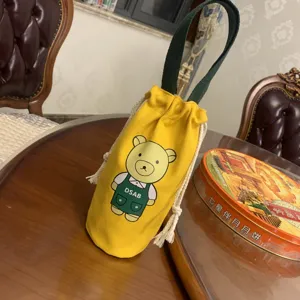 Détail de sac cordon de tasse à eau en toile cartoon jaune, motif d'ours mignon et poignée verte.