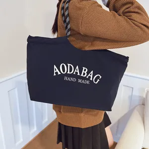 Gedetailleerd overzicht van zwarte stoffen tote bag met witte letterprint en handvat.
