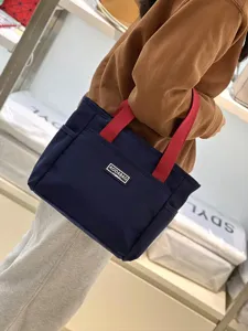 Canvas tote bag with contrast red handles, front pocket design, perfect for work and daily use.